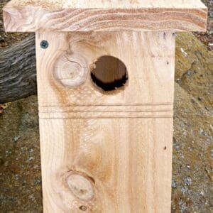 A wooden birdhouse with a round hole and roof.