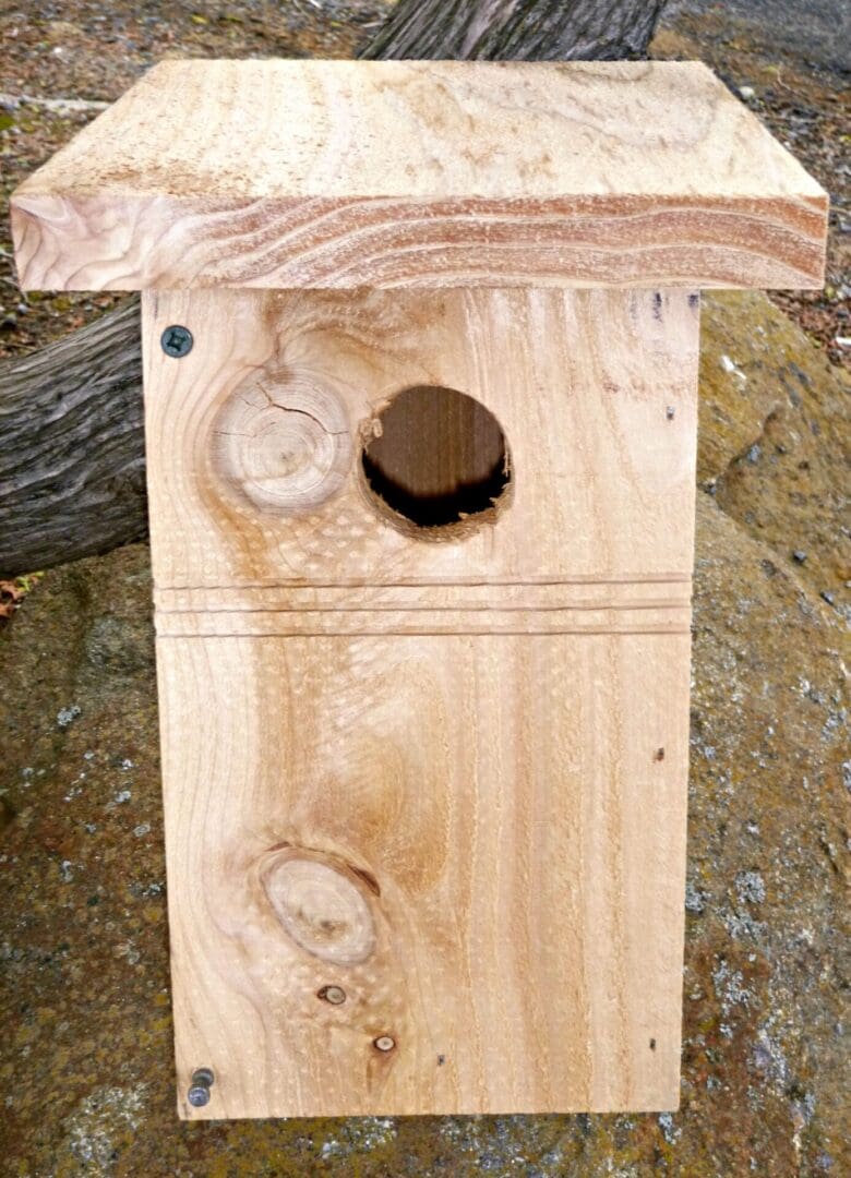 A wooden birdhouse with a round hole and roof.