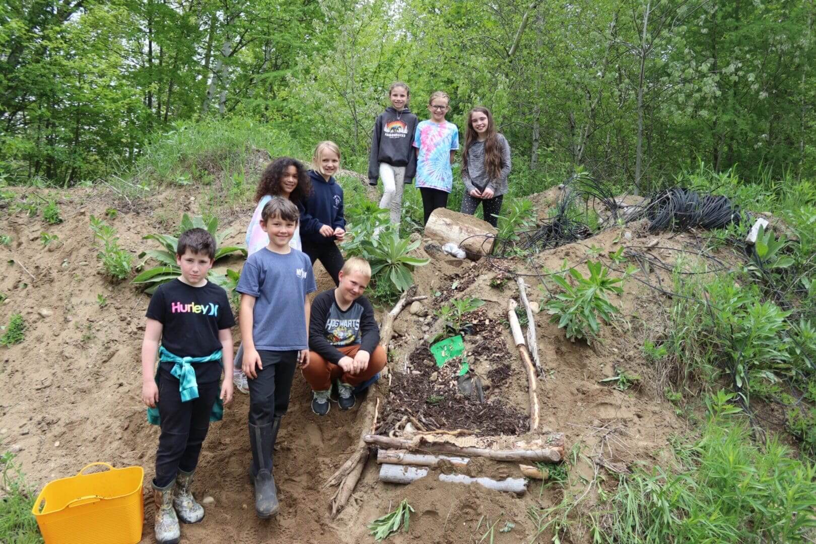 Group of children posing with a large outdoor skeleton art project in the woods.
