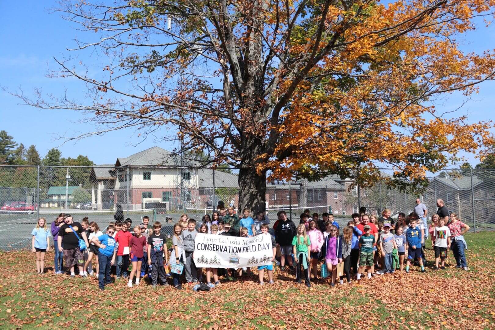 Group of children outdoors with a banner under a tree in autumn.