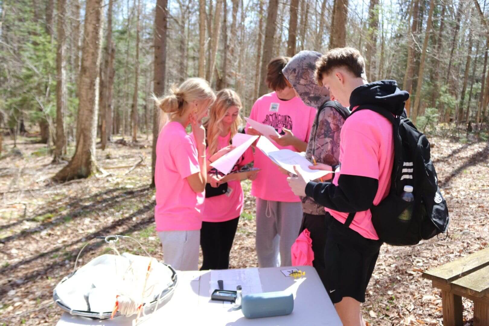 Four women in bright pink shirts discussing a map in a wooded area.